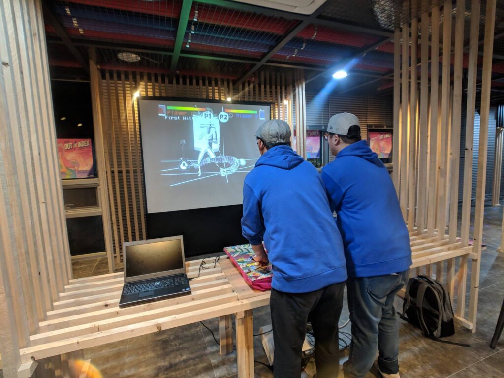 Over the shoulder shot of two men in blue hoodies playing a fighting game.