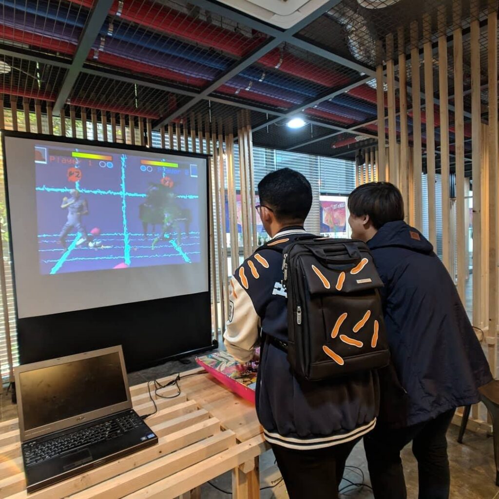 Over the shot shoulder of two men playing a fighting game. The fighting game screen is wavy.