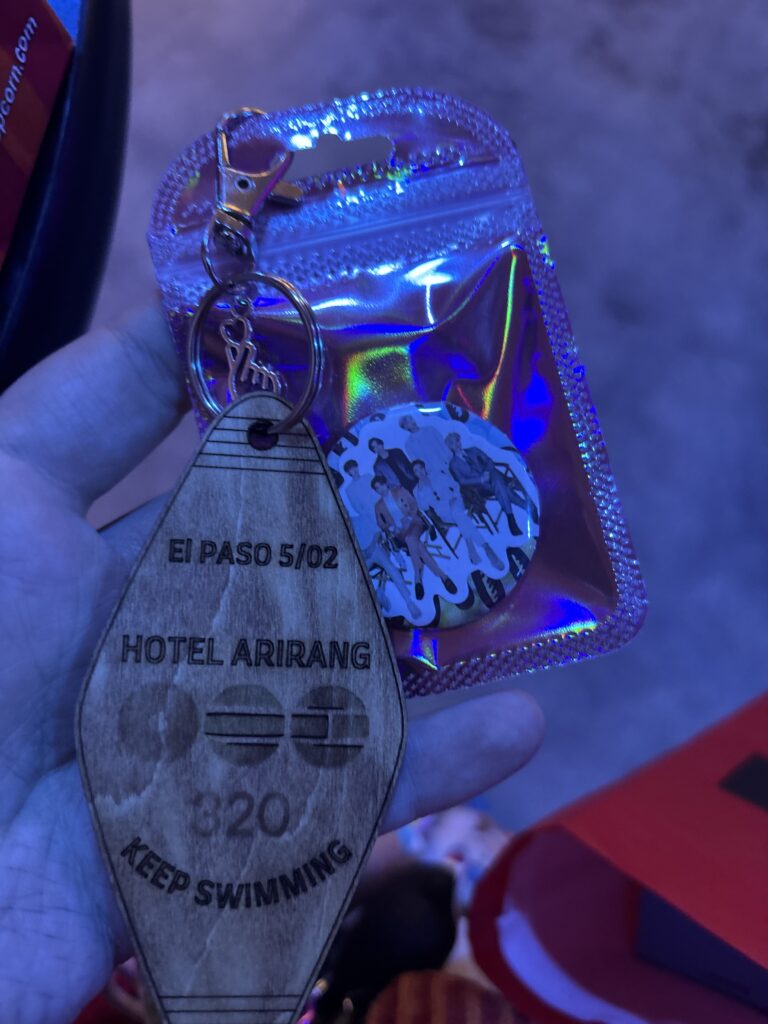 In a hand, a small keychain looking like a motel keychain and a pink bag with a pin back button in it.