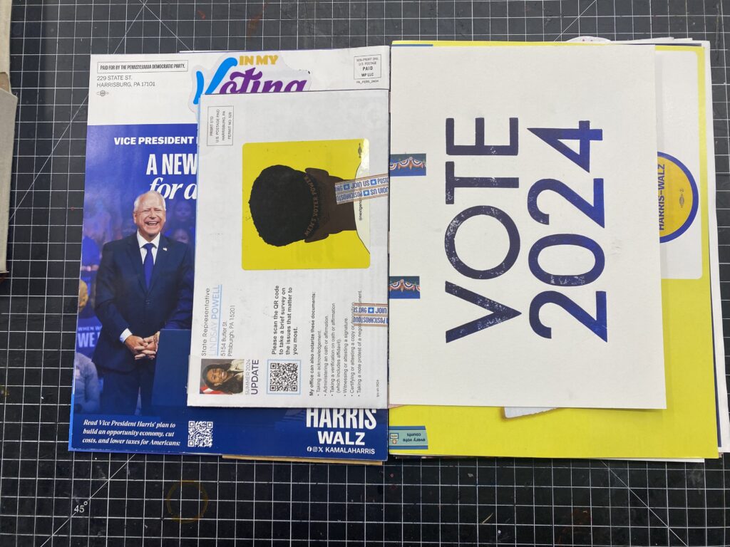 The book held open showing a letterpress printed image that says Vote 2024 and a postcard with a sticker concealing the address.