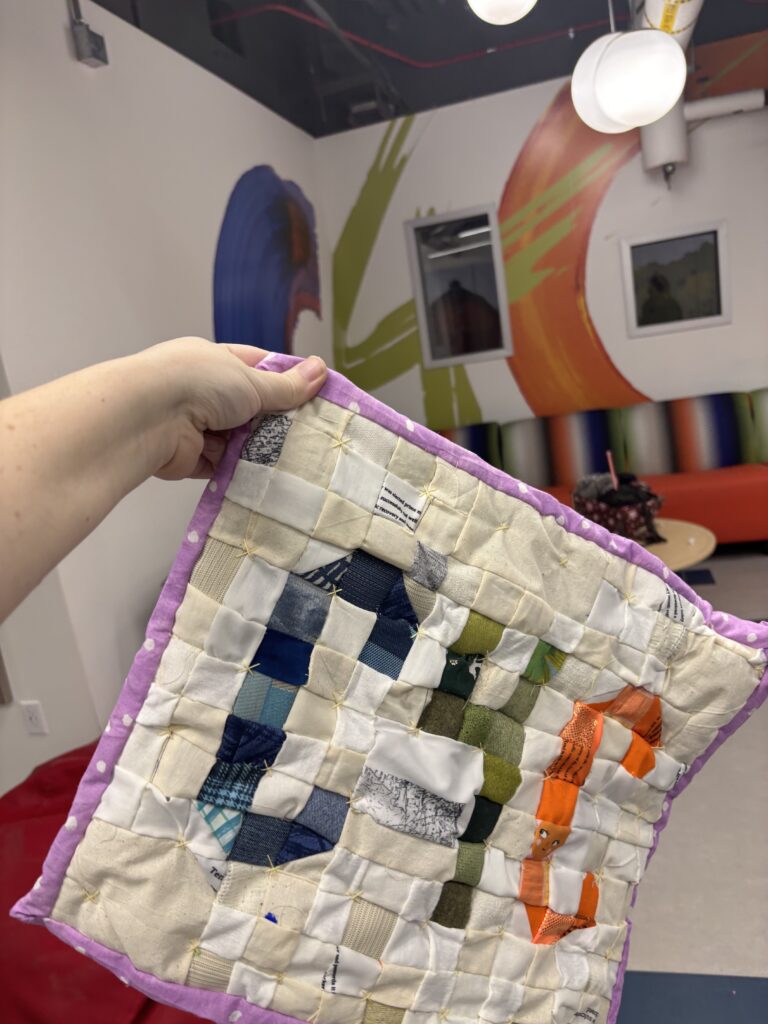 A hand showing a quilt that says C4C with a matching logo behind it with the colors matching - blue, green and then orange.