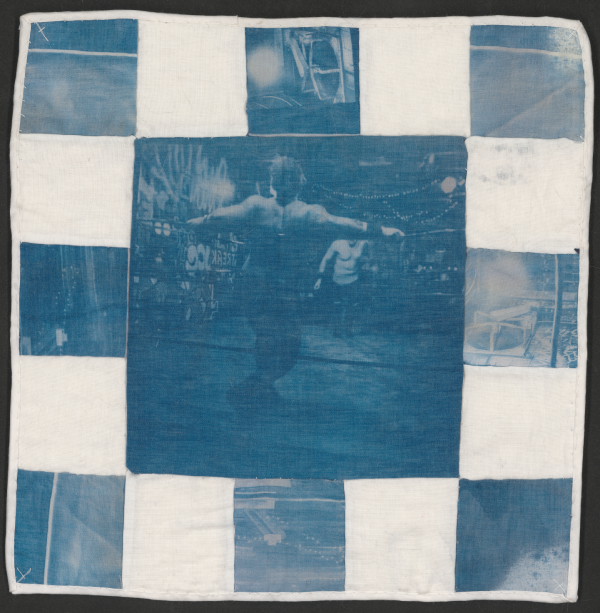 A scan of a square quilted tapestry in white and cyanotype blue. The center panel is a wrestler from behind, stretched across the top rope.